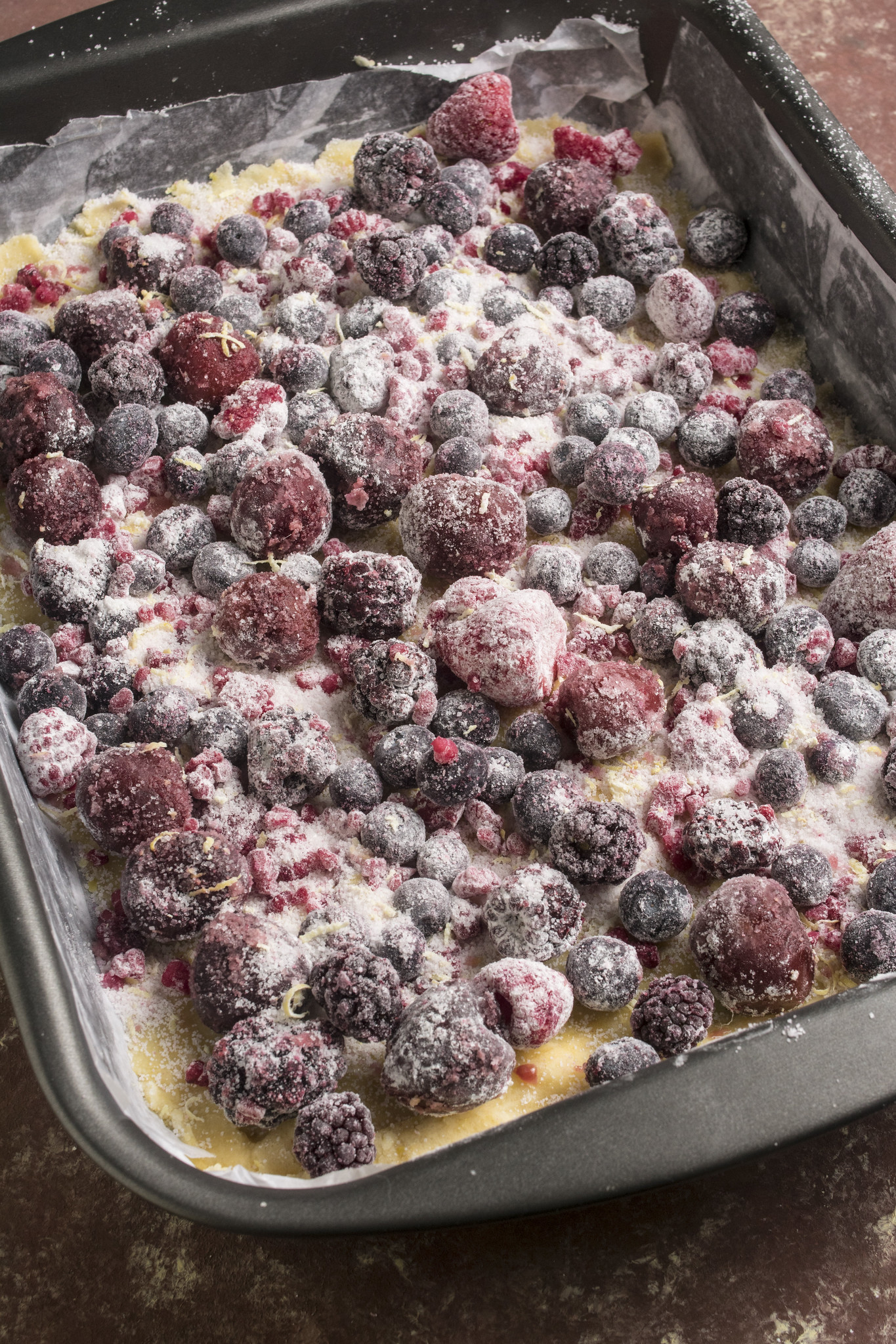Frozen fruits of the forest spread over a crumb base in a lined tin, ready to be topped for an Italian berry crumble tart.